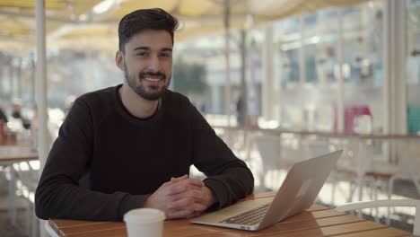 Young-man-using-laptop-and-smiling-at-camera